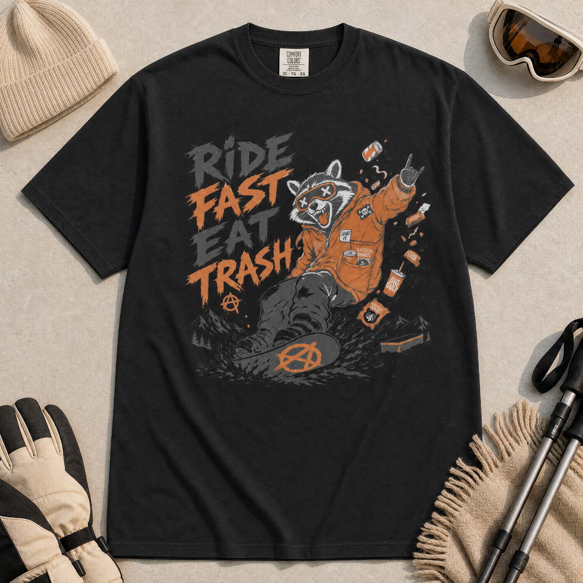 Black t-shirt with graphic design of a raccoon in an orange jacket and text 'Ride Fast Eat Trash' on a beige surface.