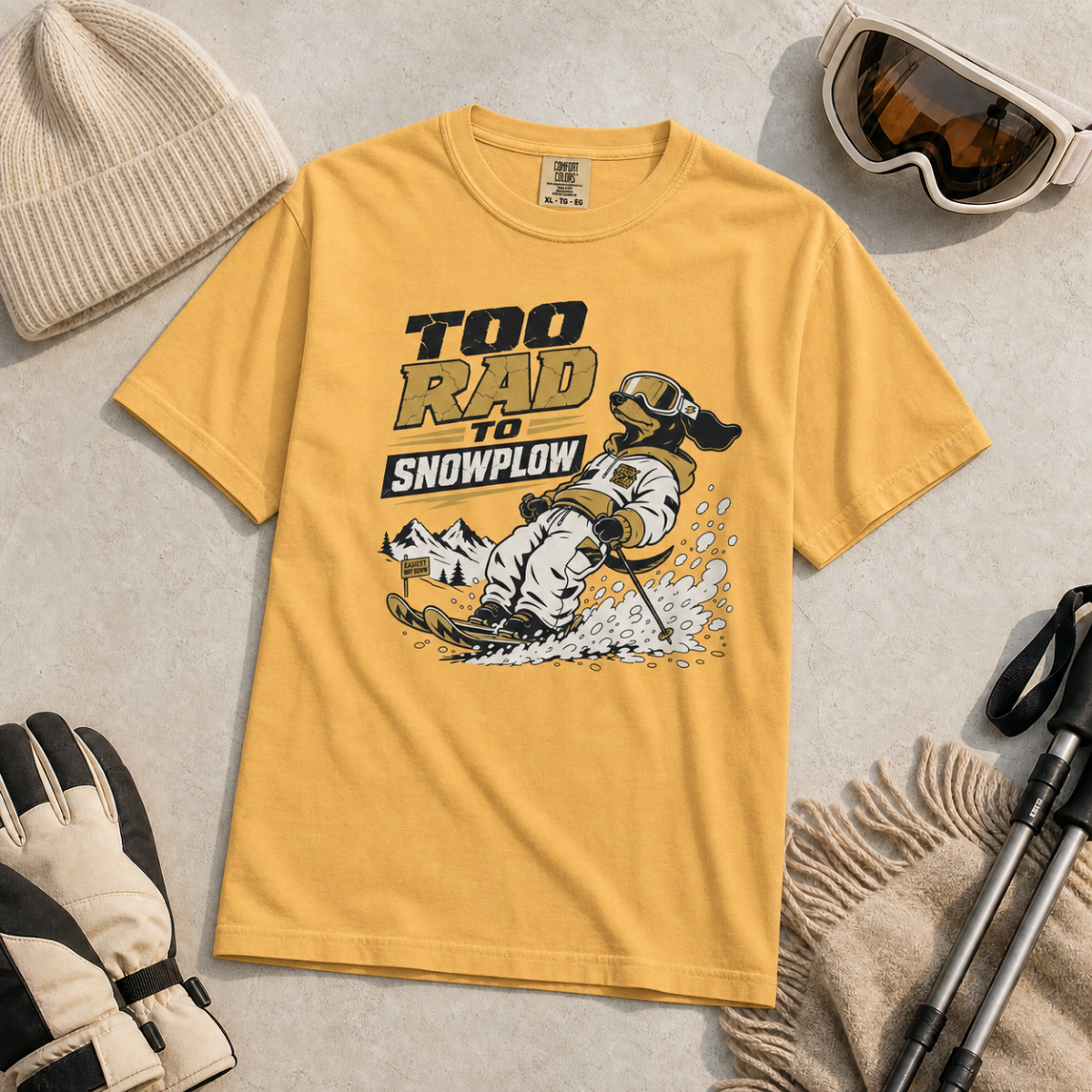 Mustard yellow t-shirt with a graphic design and text, surrounded by winter accessories on a light background