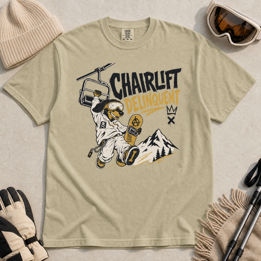 Bay green t-shirt with a graphic design featuring a dachshund snowboarder and 'Chairlift Delinquent' text, surrounded by winter accessories.