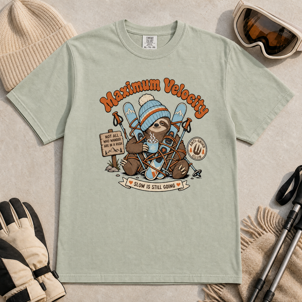 Bay green t-shirt with a sloth graphic and 'Maximum Velocity' text, surrounded by winter accessories on a beige background.