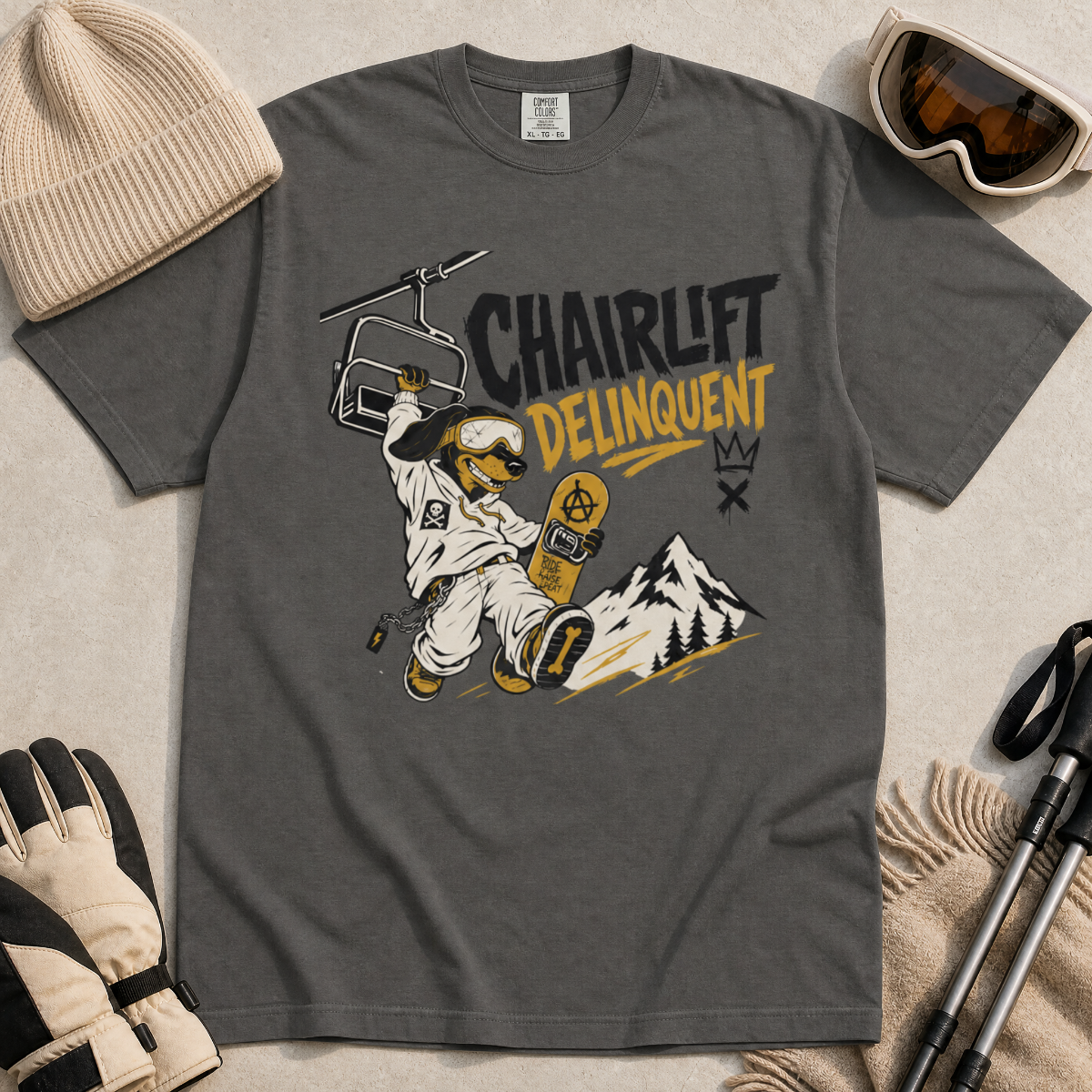 Pepper gray t-shirt with a graphic design featuring a dachshund snowboarder and 'Chairlift Delinquent' text, surrounded by winter accessories.