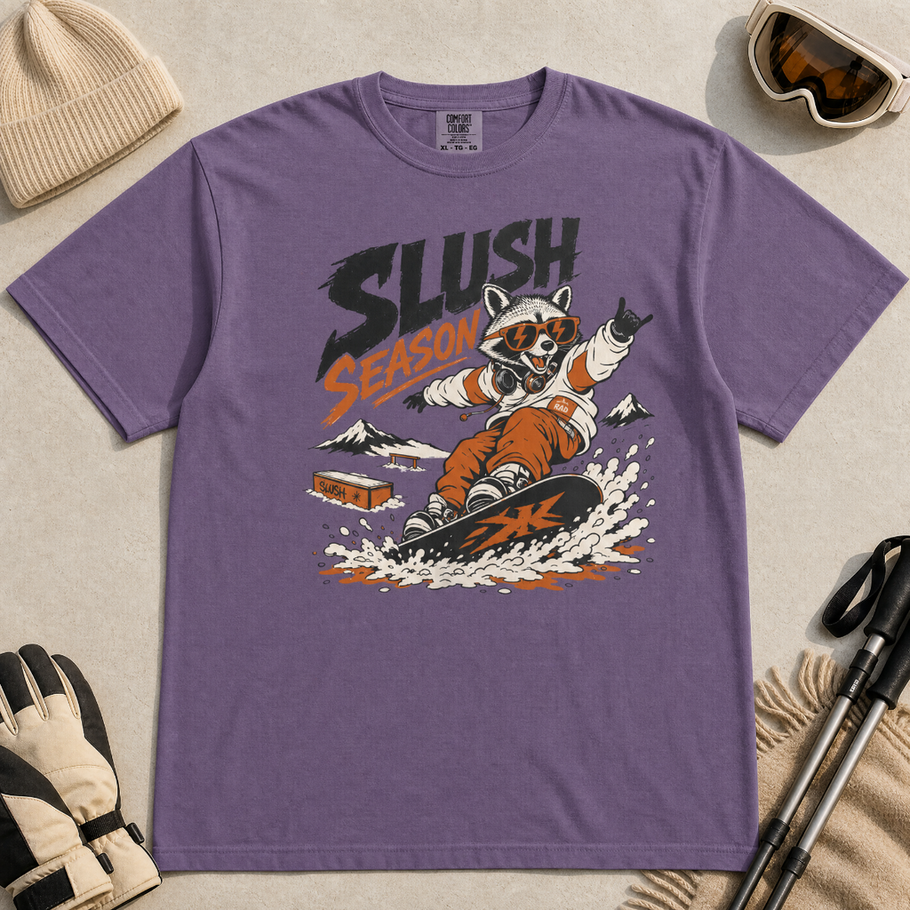 Grape purple colored t-shirt with a graphic of a raccoon snowboarding and 'Slush Season' text, surrounded by winter accessories.