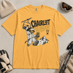 Mustard yellow t-shirt with a graphic design featuring a dachshund snowboarder and 'Chairlift Delinquent' text, surrounded by winter accessories.
