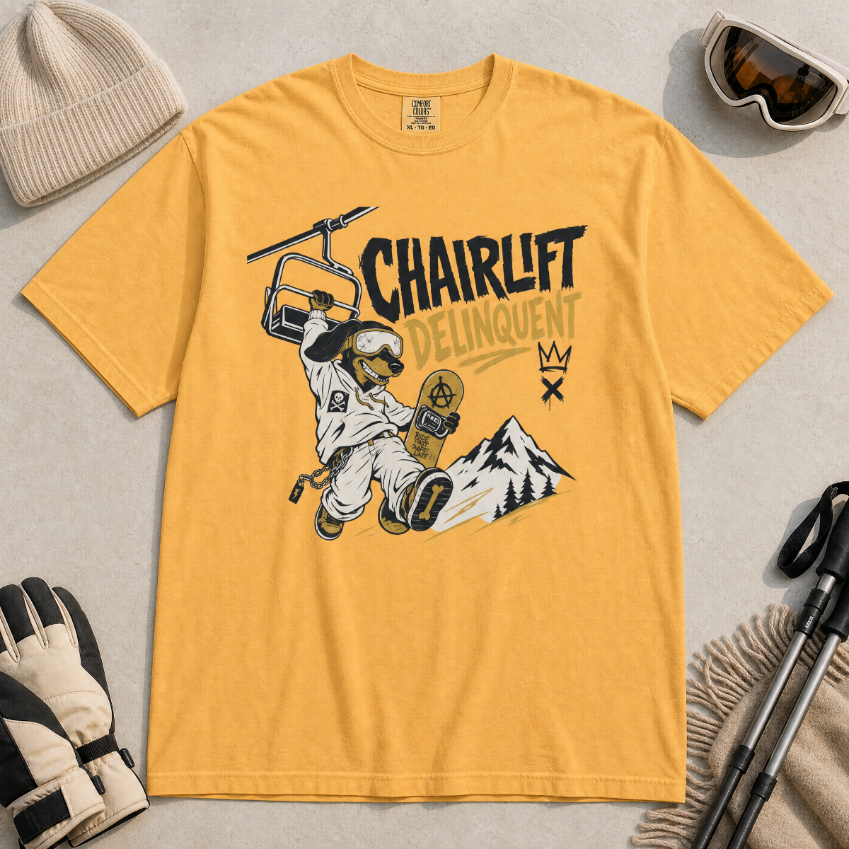 Mustard yellow t-shirt with a graphic design featuring a dachshund snowboarder and 'Chairlift Delinquent' text, surrounded by winter accessories.