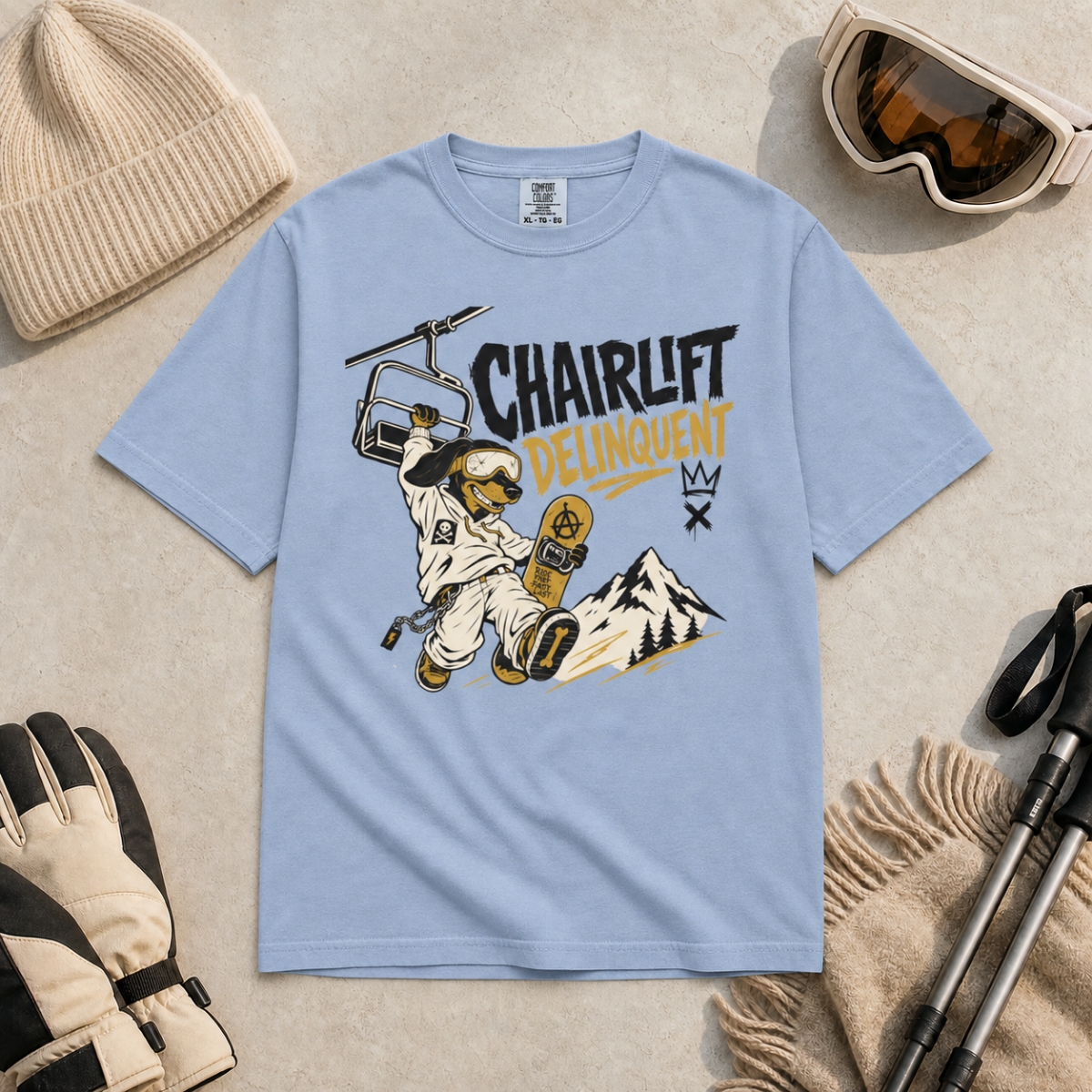 Washed denim blue t-shirt with 'Chairlift Delinquent' graphic design on a beige surface with winter accessories.