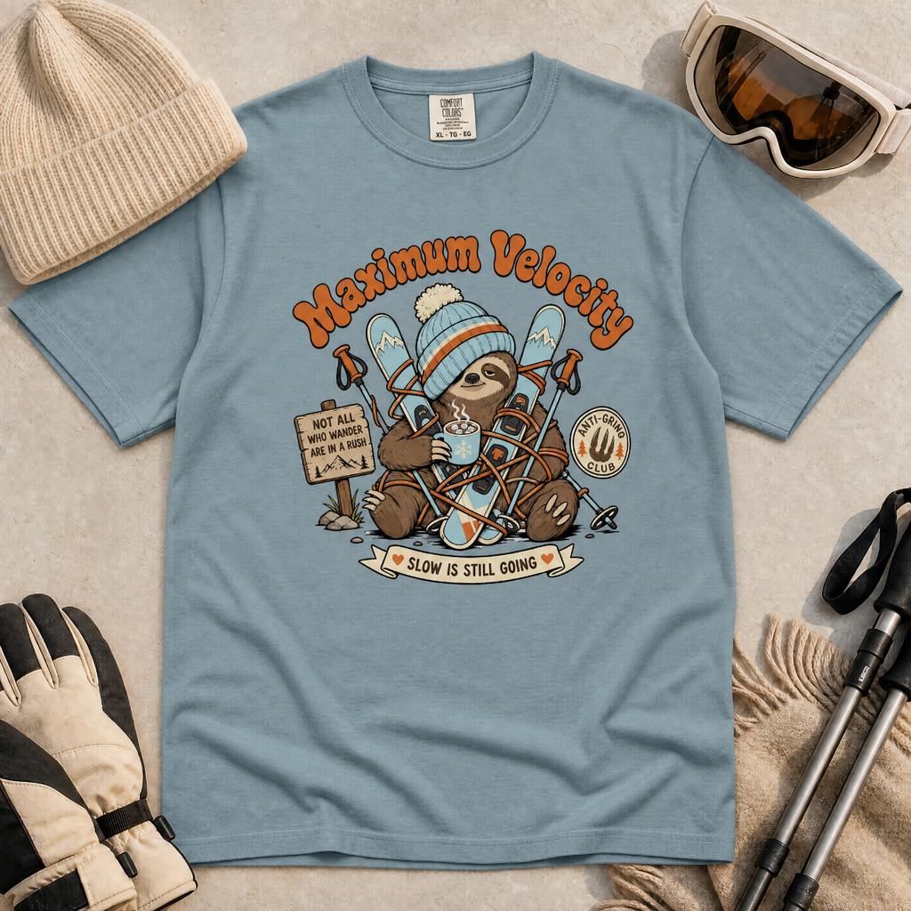 Ice blue t-shirt with a sloth graphic and 'Maximum Velocity' text, surrounded by winter accessories on a beige background.