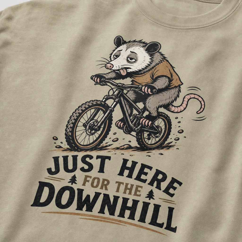 Khaki colored t-shirt with an opossum riding a bike graphic and text 'Just Here for the Downhill'.