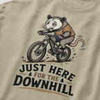 Khaki colored t-shirt with an opossum riding a bike graphic and text 'Just Here for the Downhill'.
