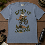Blue jean colored t-shirt with an otter on a bike graphic and text 'Send it for the snacks'.