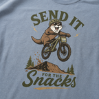 Blue jean colored t-shirt with an otter on a bike graphic and text 'Send it for the snacks'.