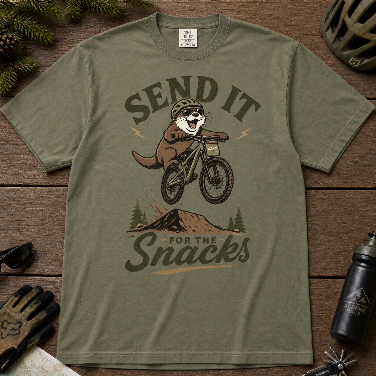 Moss green t-shirt with a graphic of an otter on a bike and text 'Send it for the snacks'.