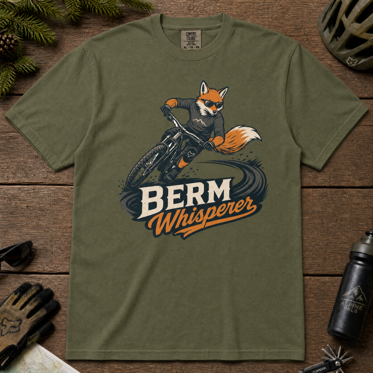 Hemp green t-shirt with a graphic of a fox riding a bike and ' Berm Whisperer'.