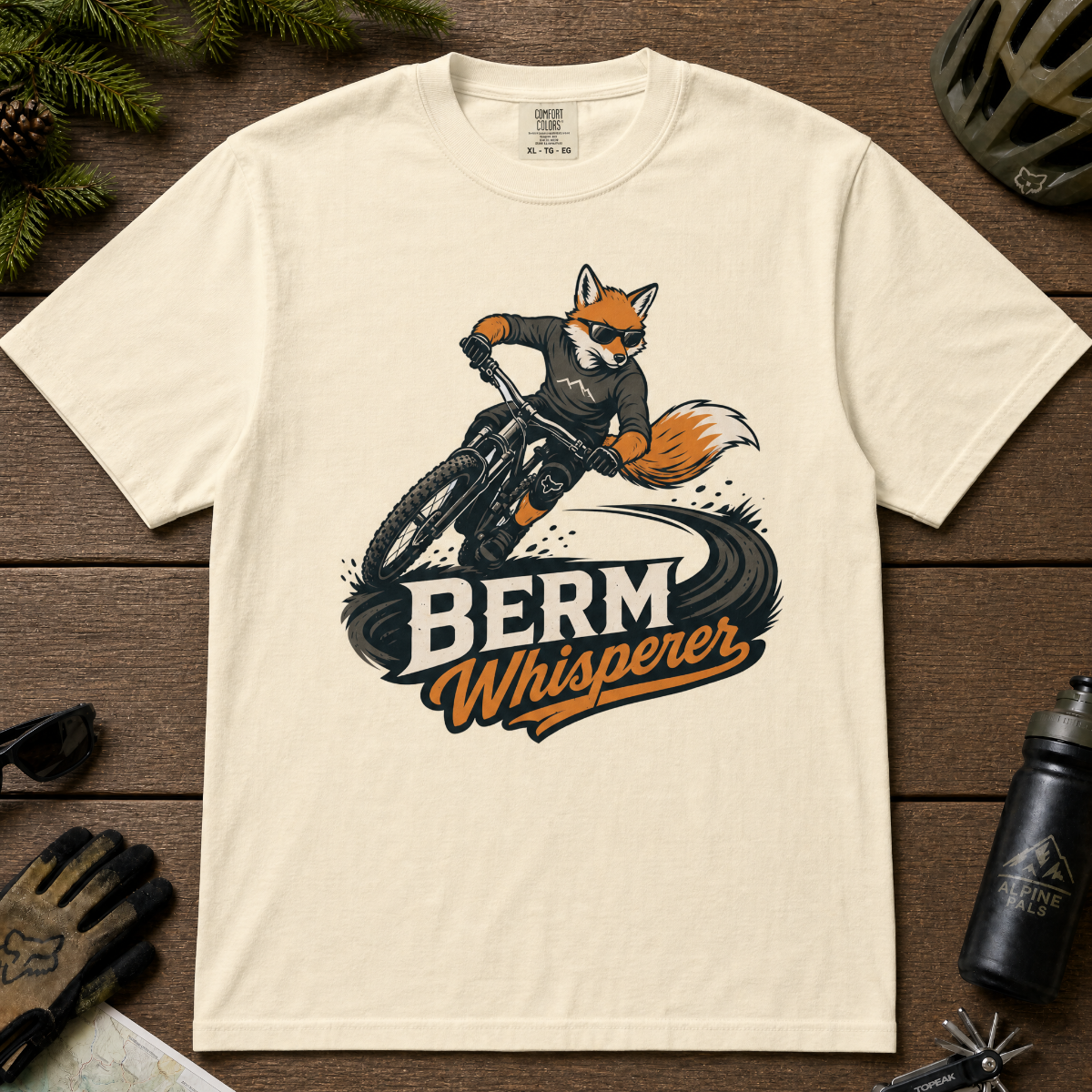 Ivory white t-shirt with a graphic of a fox riding a bike and ' Berm Whisperer'.
