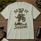 Bay green t-shirt with an otter riding a bike graphic and text 'Send it for the snacks'.
