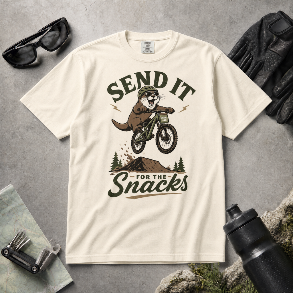 Ivory white t-shirt with graphic of an otter on a bike and text 'Send it for the snacks'.
