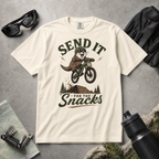 Ivory white t-shirt with graphic of an otter on a bike and text 'Send it for the snacks'.