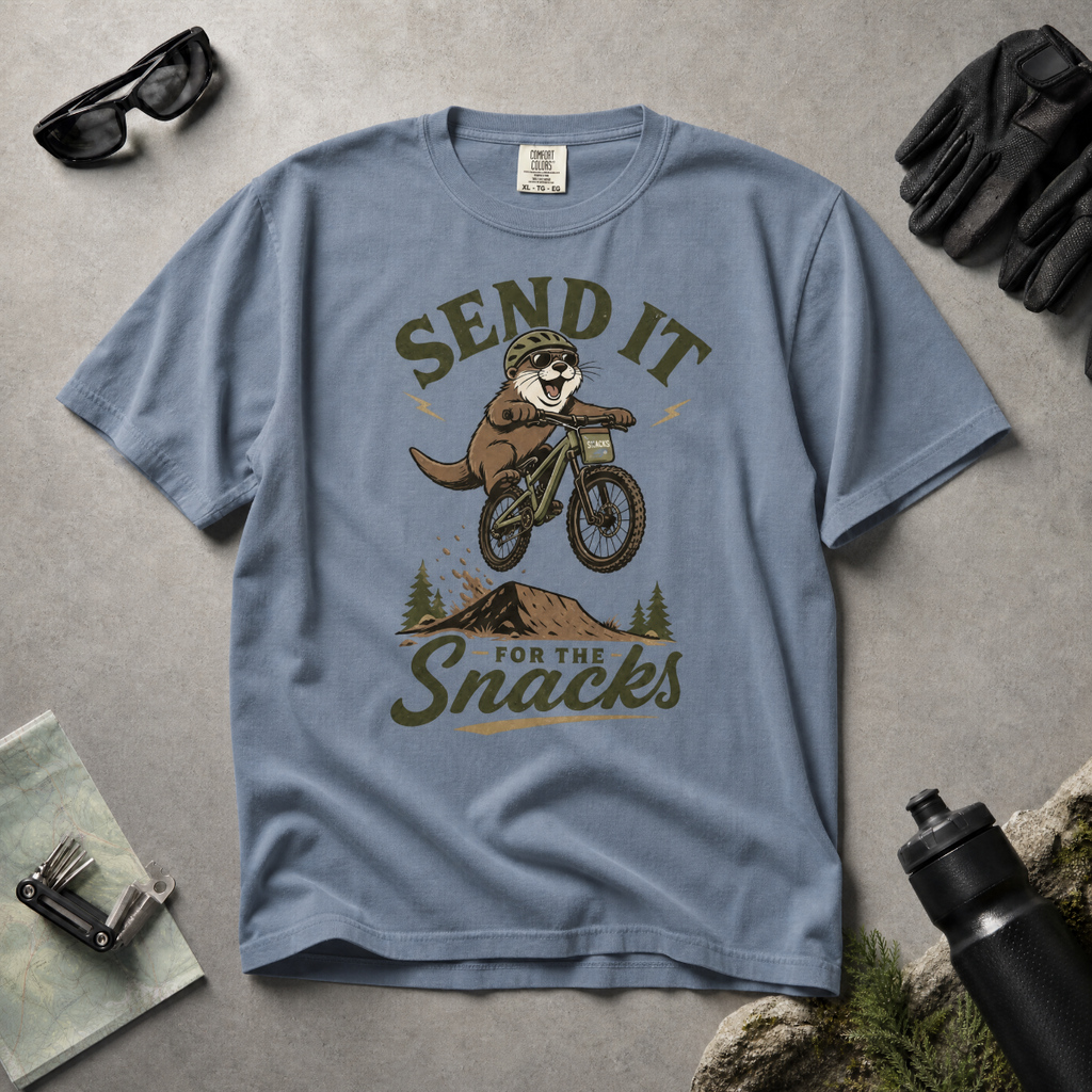 Blue jean colored t-shirt with an otter on a bike graphic and text 'Send it for the snacks'.