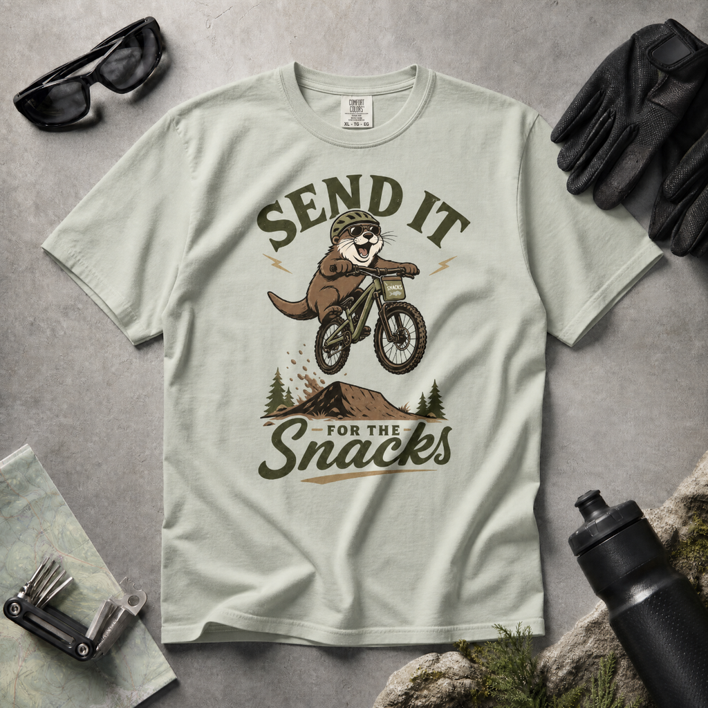 Bay green t-shirt with an otter riding a bike graphic and text 'Send it for the snacks'.