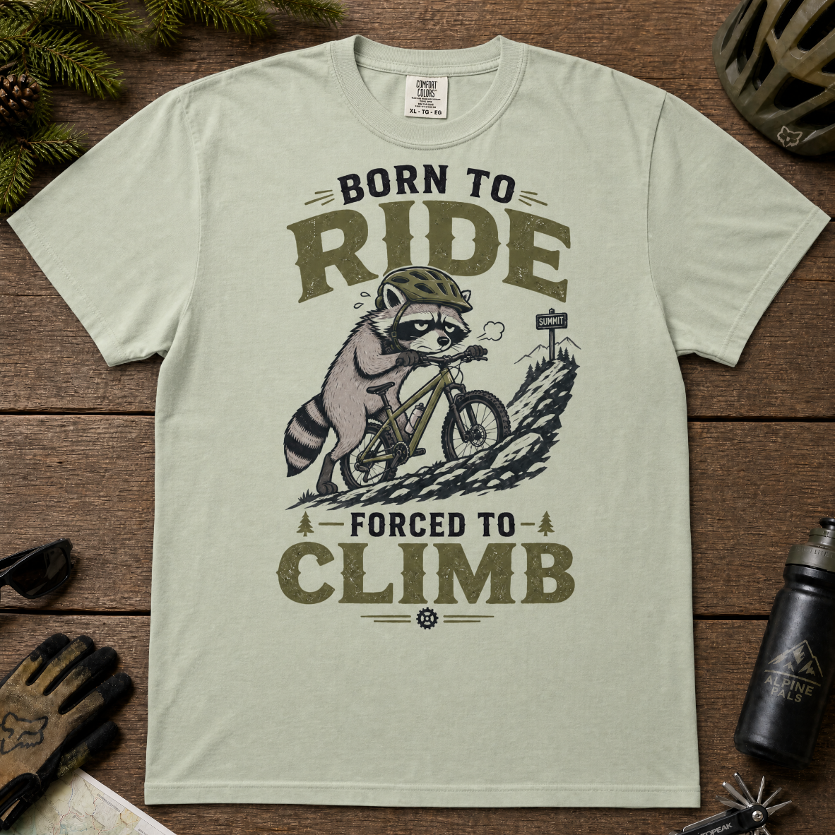 Bay green t-shirt with a graphic of a raccoon riding a bike and text 'Born to Ride, Forced to Climb'.