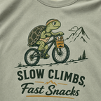 Bay green t-shirt with a graphic of a turtle riding a bike and text 'Slow Climbs, Fast Snacks'.