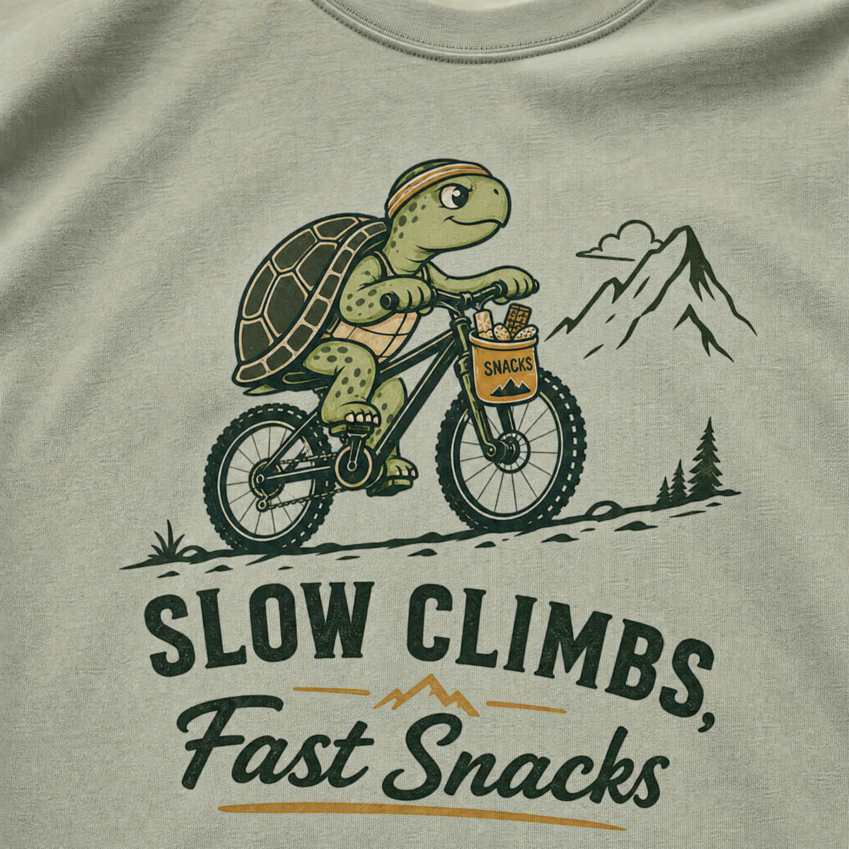 Bay green t-shirt with a graphic of a turtle riding a bike and text 'Slow Climbs, Fast Snacks'.