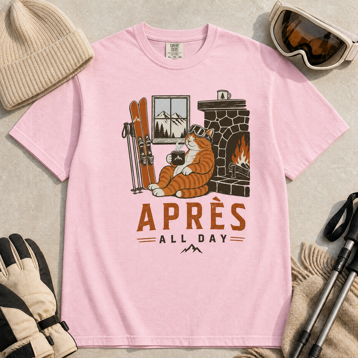 Blossom pink t-shirt with a graphic of a cat by a fireplace and skis, with 'Après All Day' text.