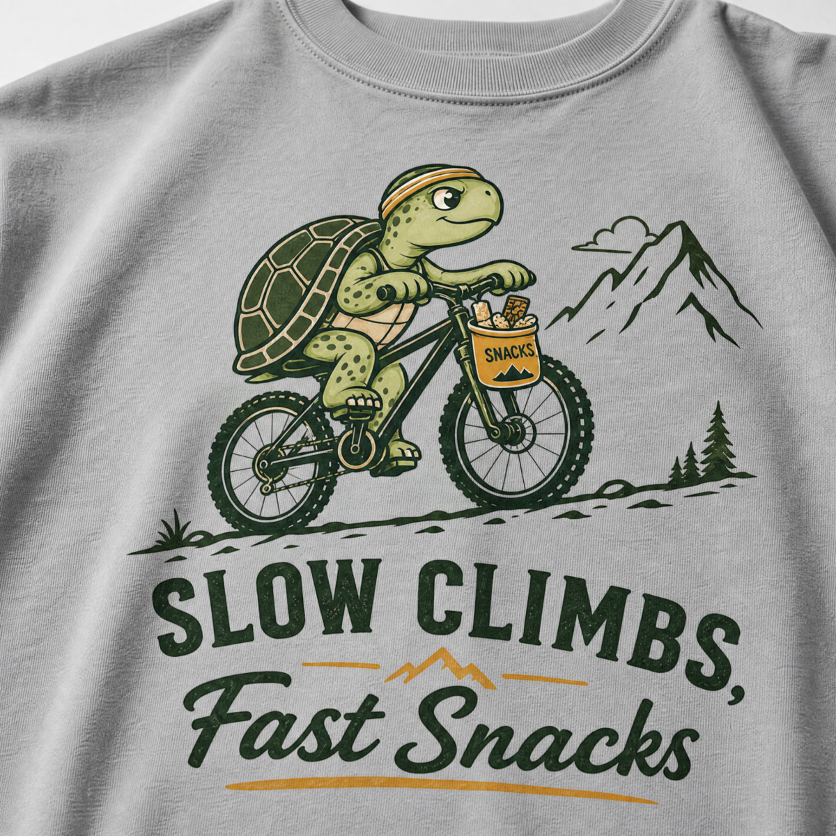 Granite colored t-shirt with a graphic of a turtle riding a bike and text 'Slow Climbs, Fast Snacks'.
