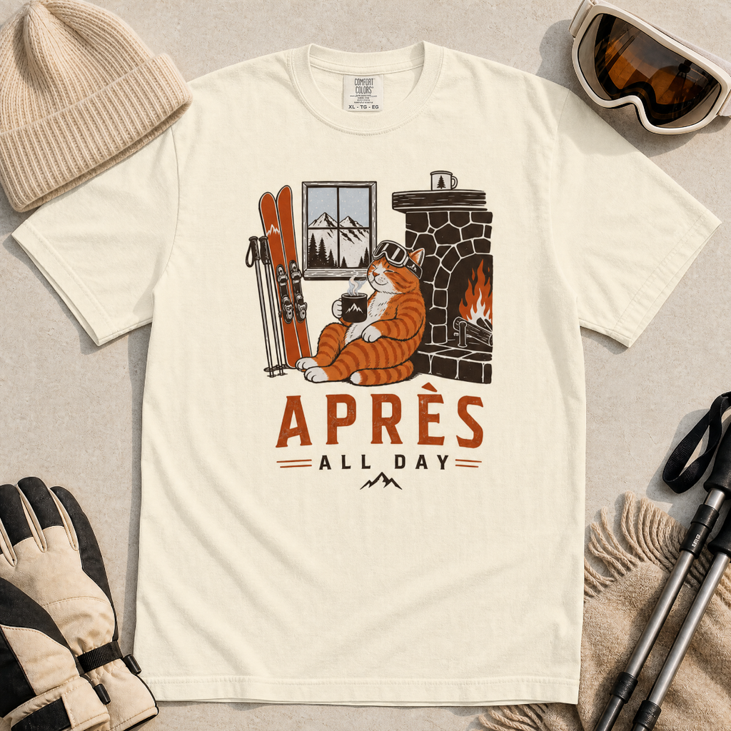 Ivory white t-shirt with a graphic of a cat by a fireplace and skis, with 'Après All Day' text.