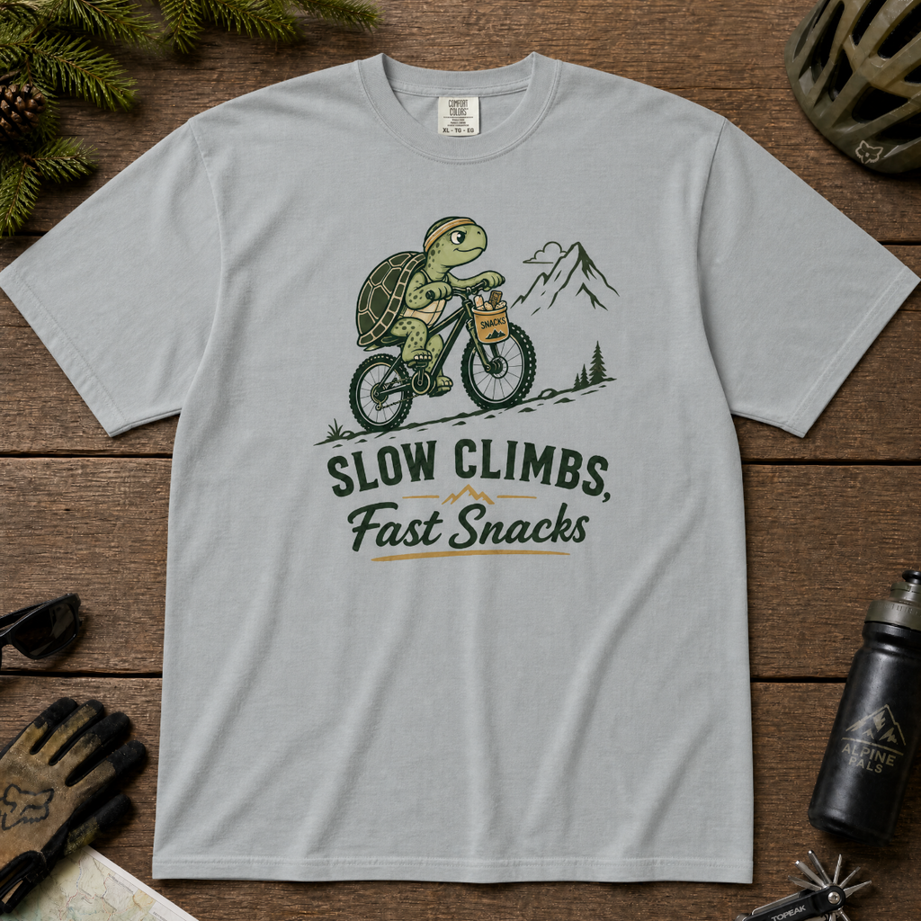Granite colored t-shirt with a graphic of a turtle riding a bike and text 'Slow Climbs, Fast Snacks'.