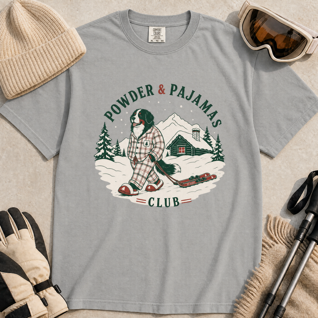 Grey t-shirt with a graphic of a dog in checkered pajamas pulling skis, trees, and a cabin, with 'Powder & Pajamas Club' text.