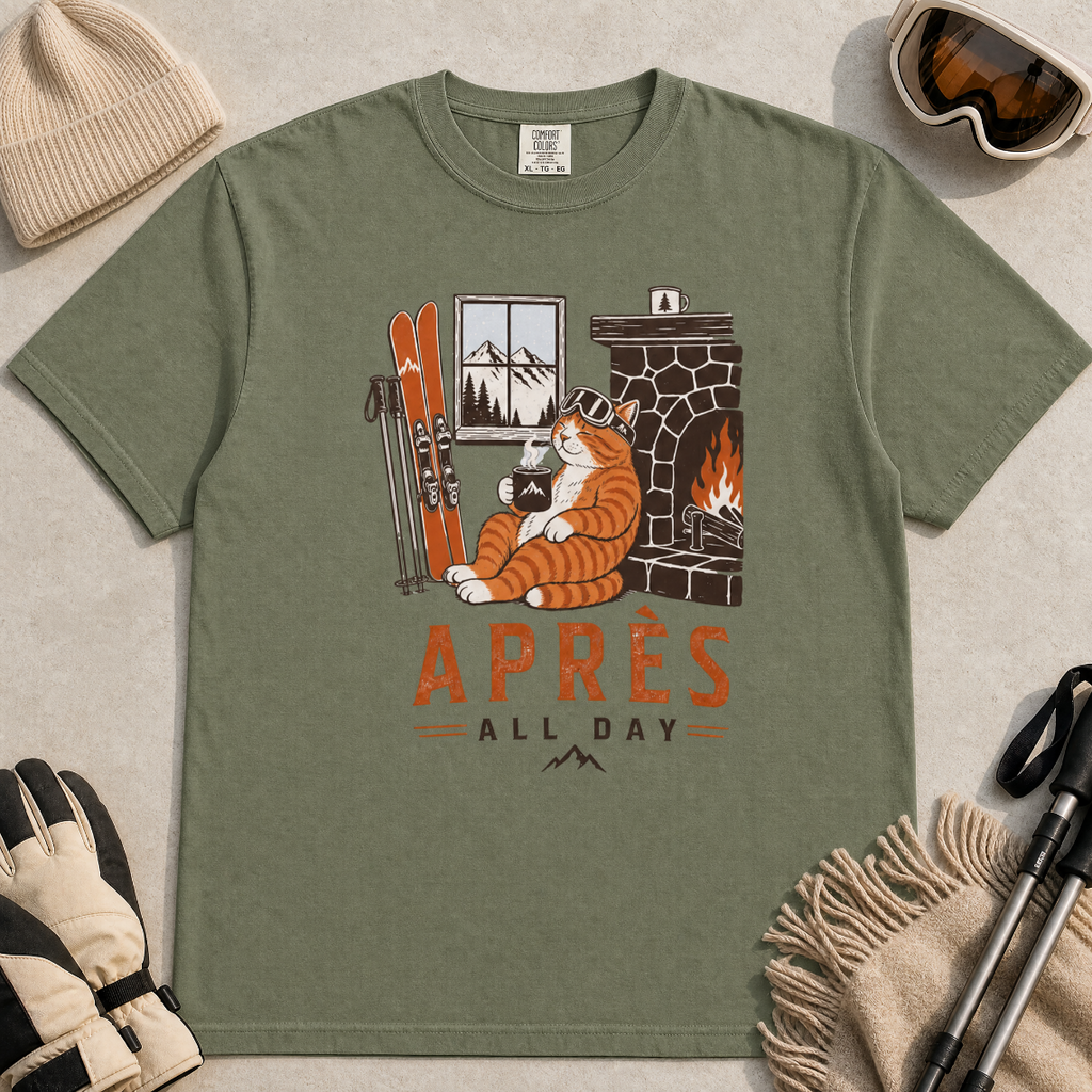 Moss green t-shirt with a graphic of a cat by a fireplace and skis, with 'Après All Day' text.