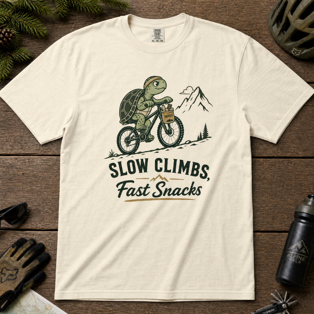 Ivory white t-shirt with a graphic of a turtle riding a bike and text 'Slow Climbs, Fast Snacks'.