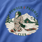 Mystic blue t-shirt with a graphic of a dog in checkered pajamas pulling skis, trees, and a cabin, with 'Powder & Pajamas Club' text.