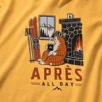 Mustard yellow t-shirt with a graphic of a cat by a fireplace and skis, with 'Après All Day' text.
