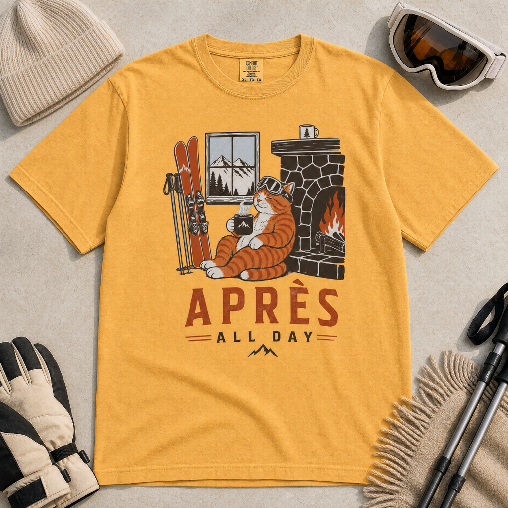 Mustard yellow t-shirt with a graphic of a cat by a fireplace and skis, with 'Après All Day' text.