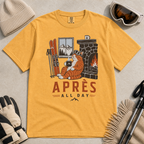 Mustard yellow t-shirt with a graphic of a cat by a fireplace and skis, with 'Après All Day' text.
