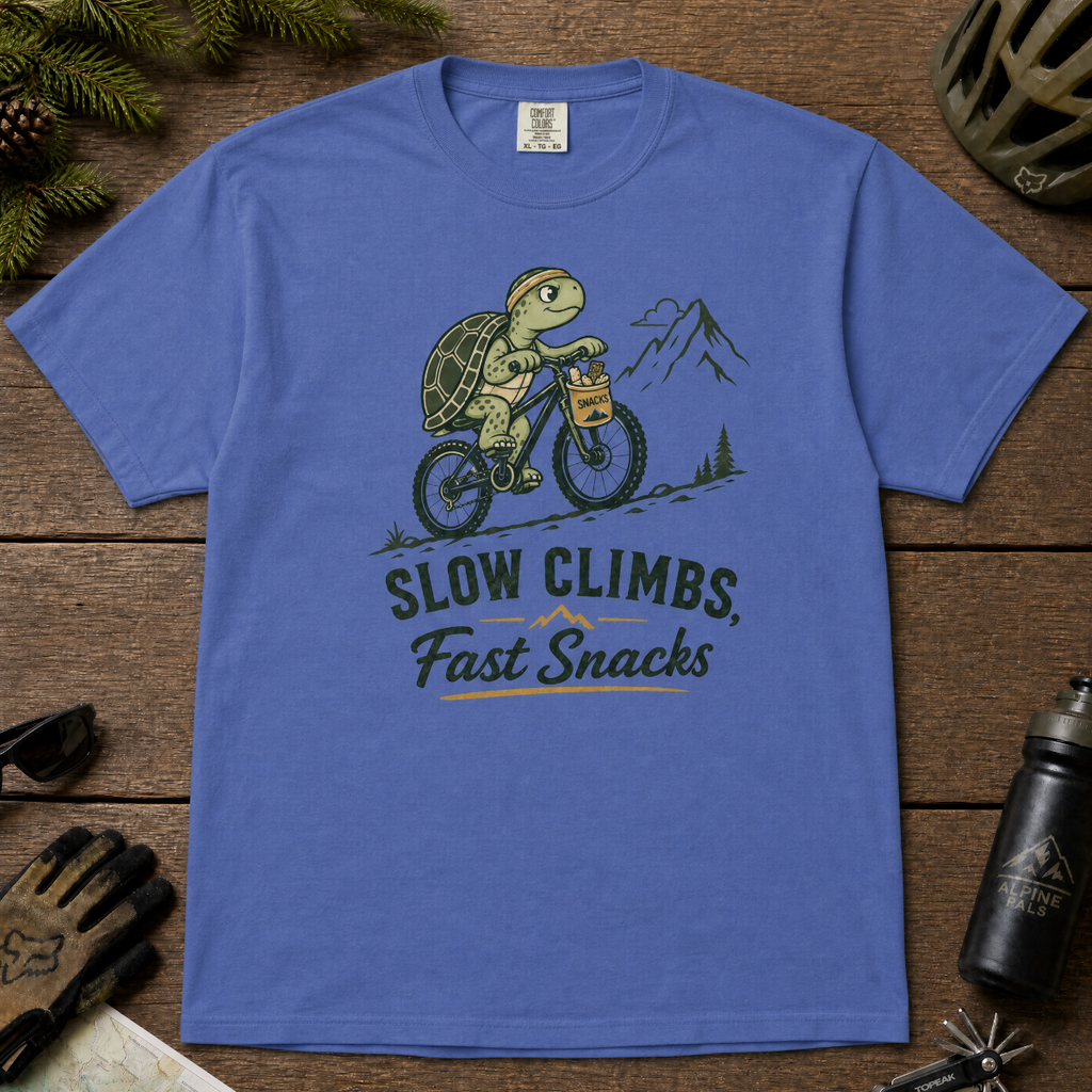 Mystic blue colored t-shirt with a graphic of a turtle riding a bike and text 'Slow Climbs, Fast Snacks'.