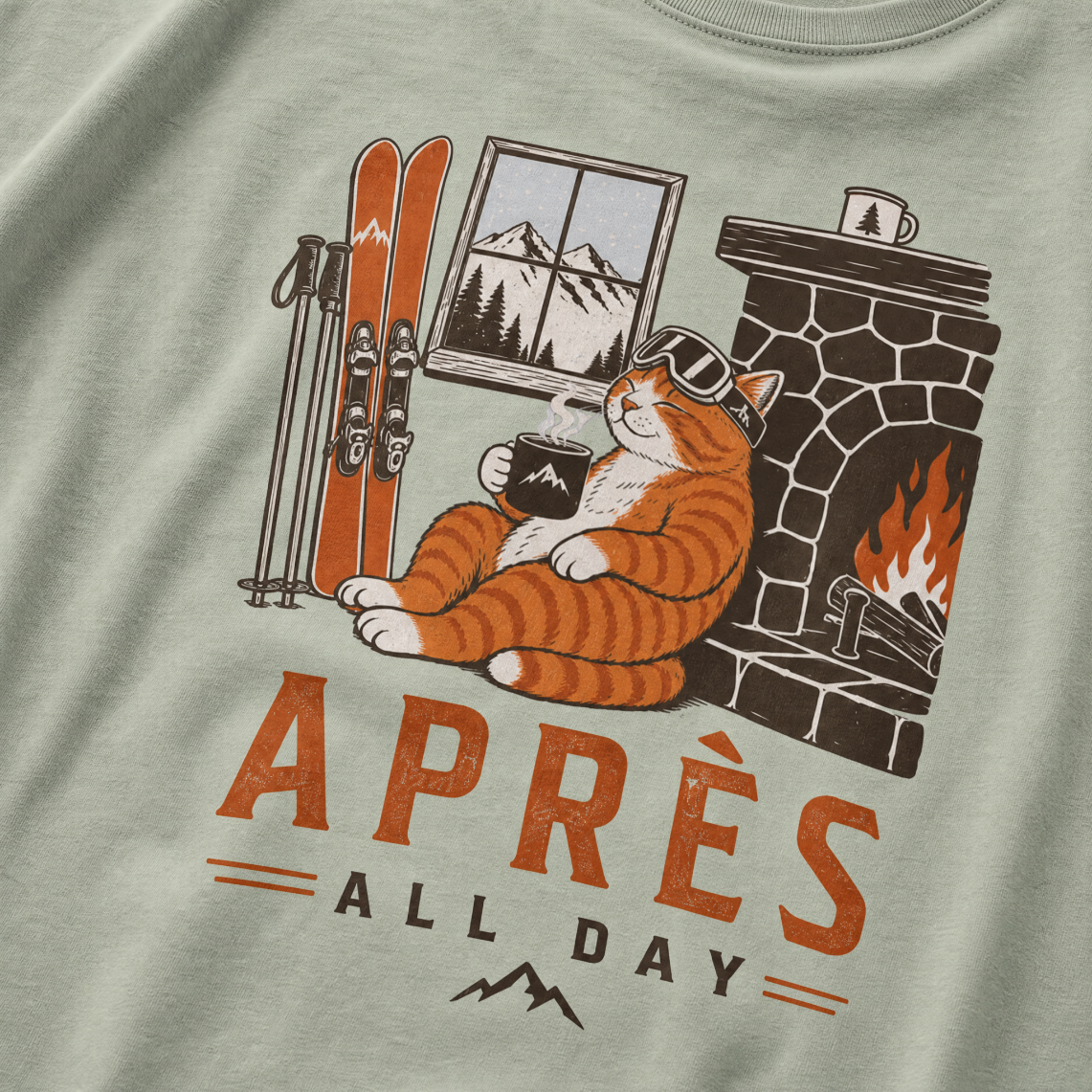 Bay green t-shirt with a graphic of a cat by a fireplace and skis, with 'Après All Day' text.