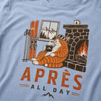 Washed denim blue t-shirt with a graphic of a cat by a fireplace and skis, with 'Après All Day' text.