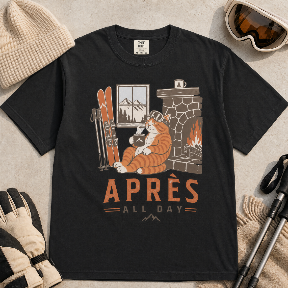 Black t-shirt with a graphic of a cat by a fireplace and skis, with 'Après All Day' text.