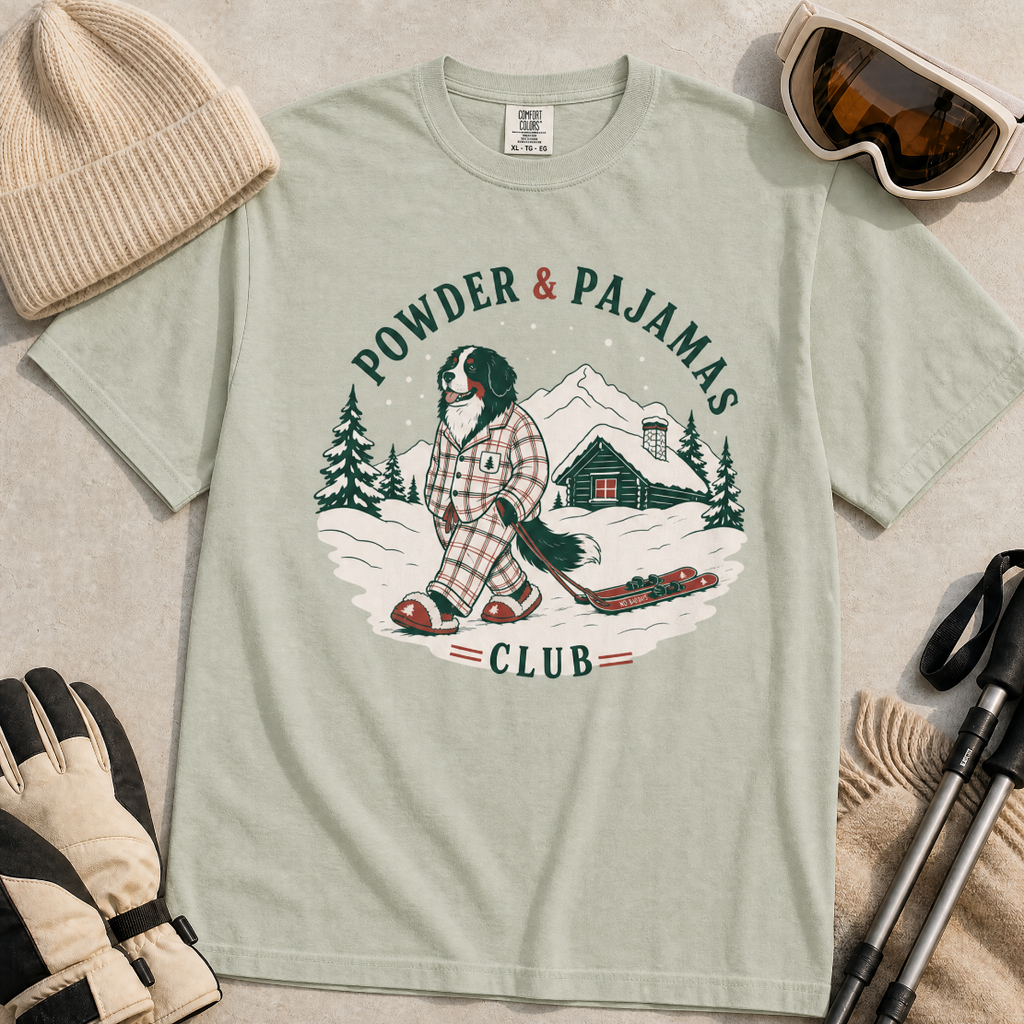 Bay green t-shirt with a graphic of a dog in checkered pajamas pulling skis, trees, and a cabin, with 'Powder & Pajamas Club' text.