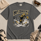 Pepper gray t-shirt with a graphic design of a dog skiing, text 'Hot Doggin', surrounded by winter accessories on a beige surface.