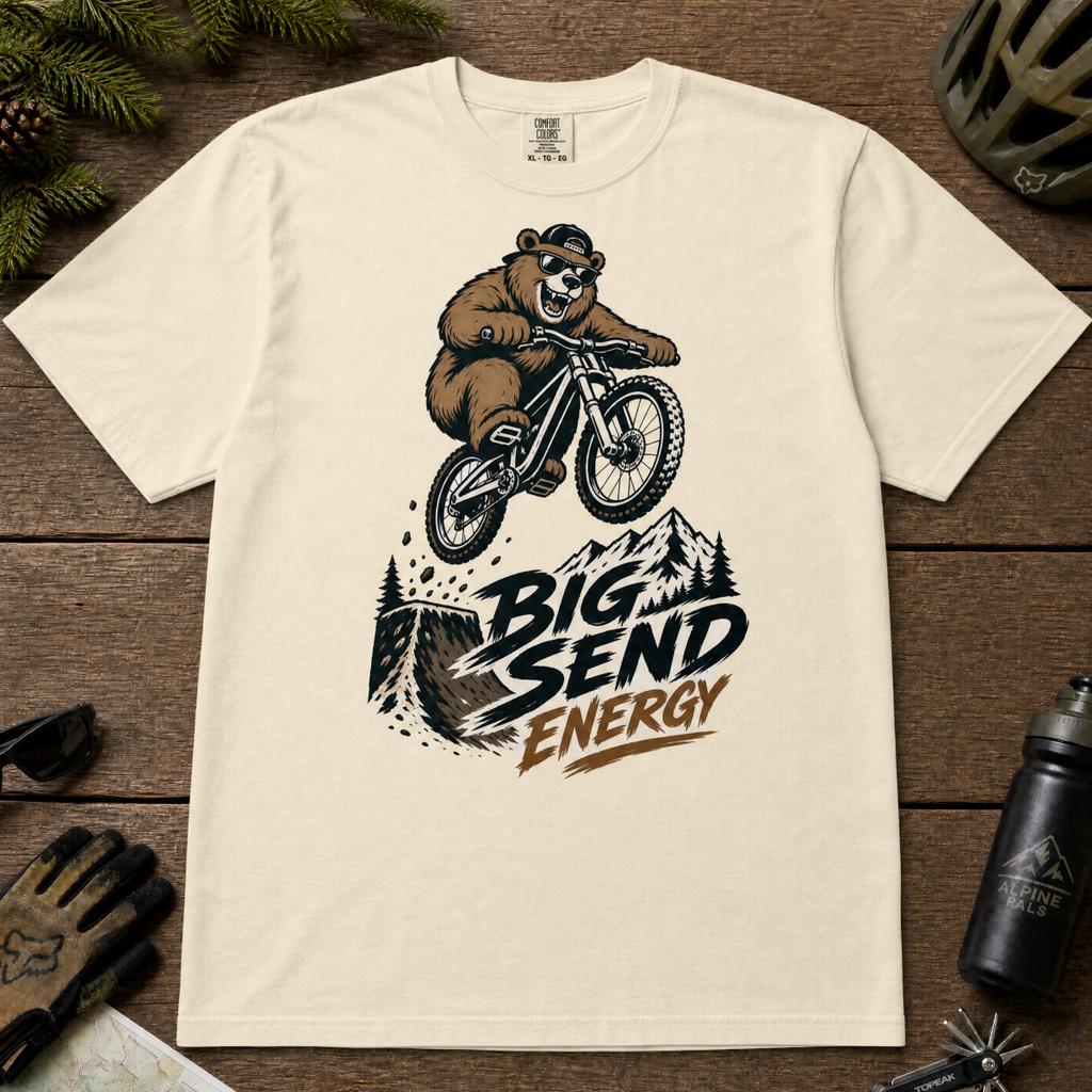 Ivory white t-shirt with bear riding a bike graphic and 'Big Send Energy' text on a wooden surface.