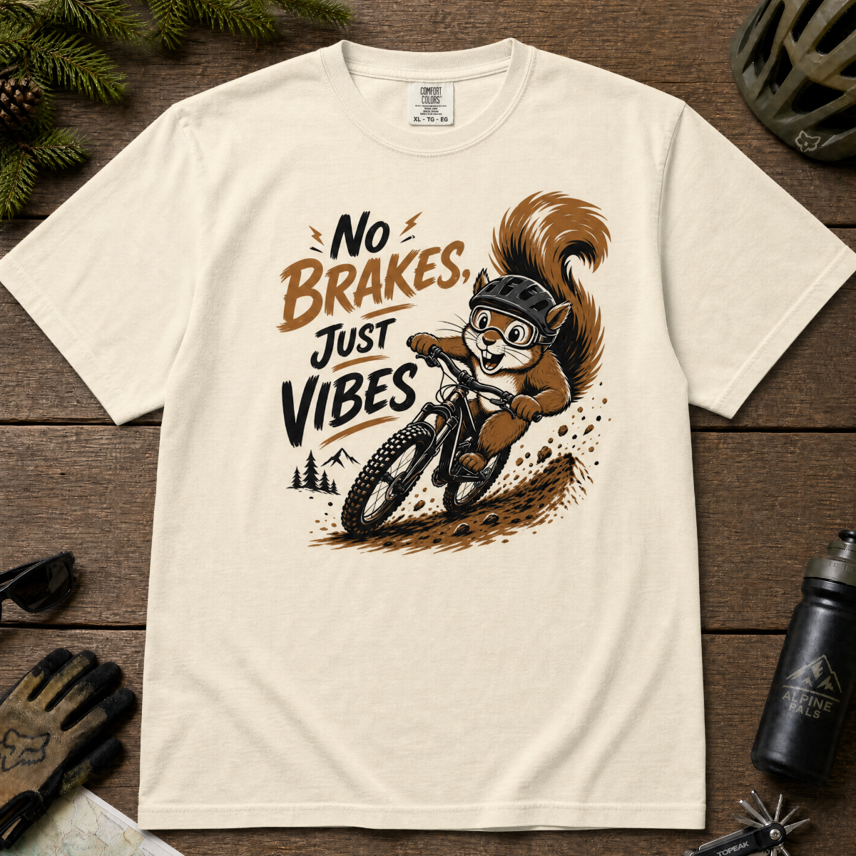 Ivory white t-shirt with a graphic of a squirrel riding a bike and text 'No Brakes, Just Vibes' on a wooden surface.