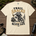 Ivory white t-shirt with a raccoon graphic and text 'Trail Snacks Were Never Safe' on a wooden surface.