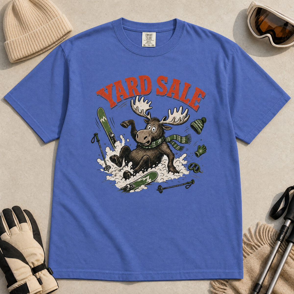 Mystic blue t-shirt with moose graphic and 'Yard Sale' text, surrounded by winter accessories on a light background