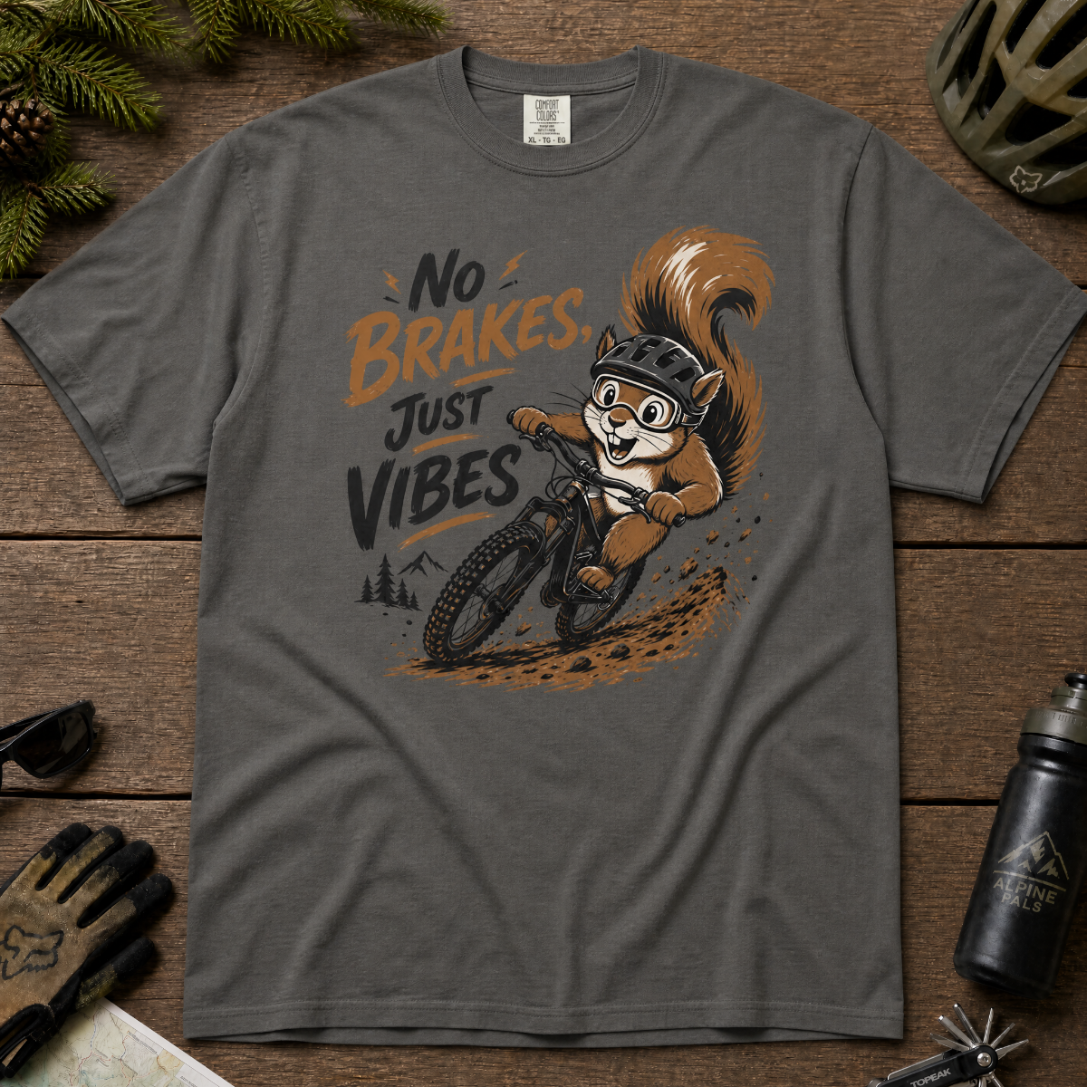 Pepper gray t-shirt with a graphic of a squirrel riding a bike and text 'No Brakes, Just Vibes' on a wooden surface.