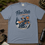 Blue jean colored t-shirt with a fox riding a bike graphic and 'Flow State Activated' text on a wooden surface.