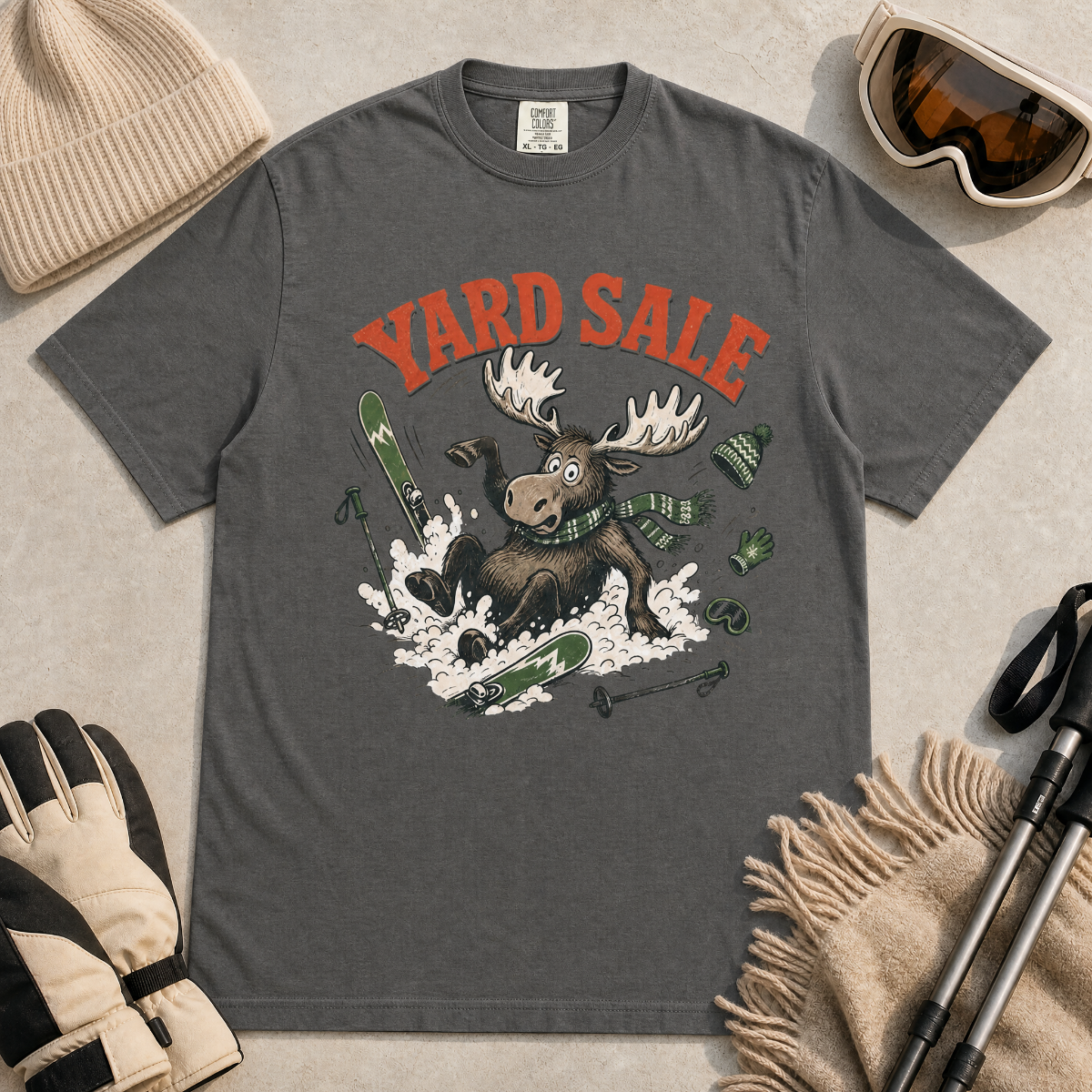 Pepper gray t-shirt with moose graphic and 'Yard Sale' text, surrounded by winter accessories on a light background