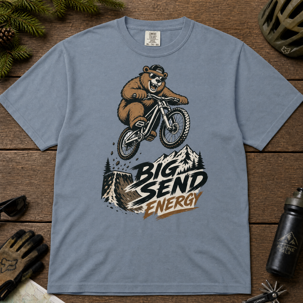 Blue jean colored t-shirt with a bear riding a bike graphic and 'Big Send Energy' text on a wooden surface.